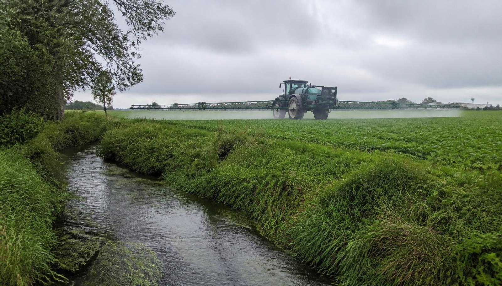 Pulvérisateur agricole traitant un champ bordé d'un cours d'eau